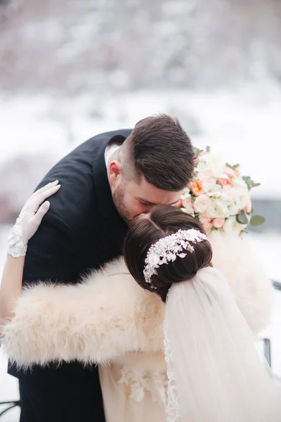 Elegantní nevěsta v bílém kožichu stojí s krásným vousatým ženichem před zasněženými stromy — Stock fotografie