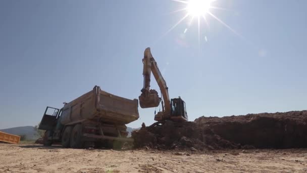 En grävmaskin gräver kol och häller det i en stor sopbil — Stockvideo