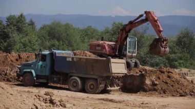 Bir kazıcı kömür kazar ve büyük bir çöp kamyonuna döker.