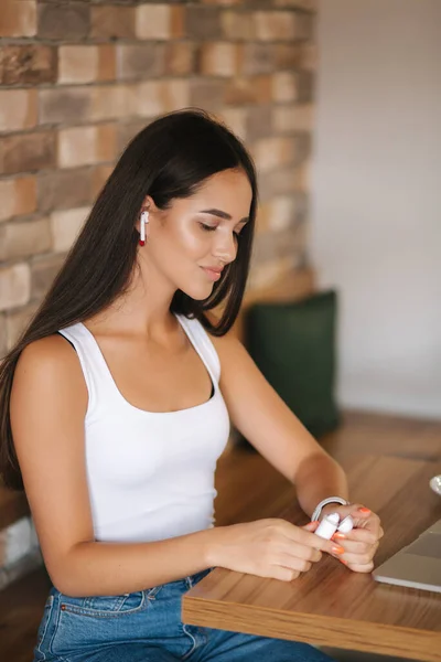 迷人的年轻女孩使用无线耳机和笔记本电脑。穿着白色T恤和斜纹棉布的女人。学生在咖啡店学习。一个人在咖啡店 — 图库照片