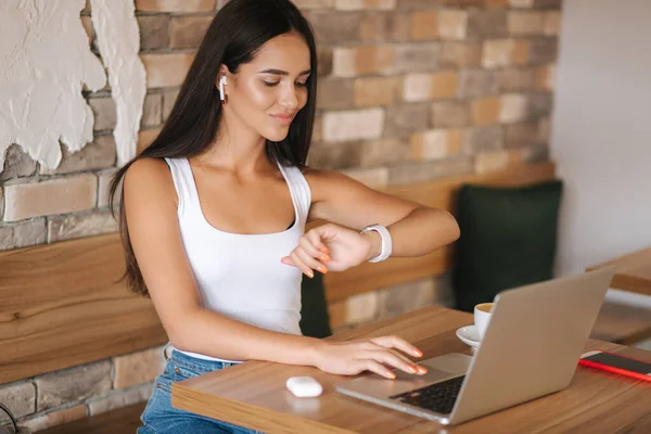 Jonge vrouw drinkt koffie en werkt op een laptop in een café. Slimme vrouw verdient online geld. Studeren in een café. Alleen in café, sociale afstand nemen — Stockfoto