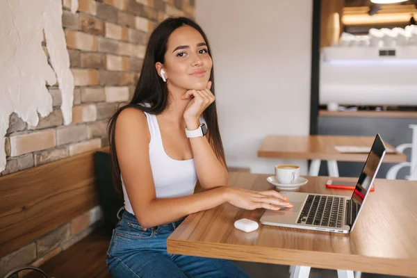 Νεαρή γυναίκα πίνει καφέ και δουλεύει σε λάπτοπ στο καφέ. Έξυπνη γυναίκα κερδίζει χρήματα σε απευθείας σύνδεση. Σπουδές σε καφετέρια. Μόνος σε καφέ, σε κοινωνική απόσταση — Φωτογραφία Αρχείου