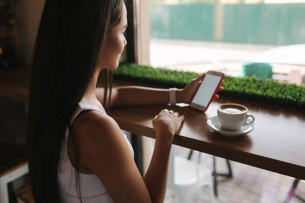 Aantrekkelijke jonge vrouw met behulp van telefoon in het café. Mooie brunette meisje chatten — Stockfoto