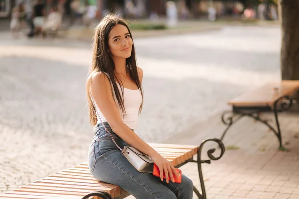 Morena atraente sentada sozinha no banco no centro da cidade. Mulher bonita bebendo café ao ar livre. Fim da quarentena. Distância social — Fotografia de Stock