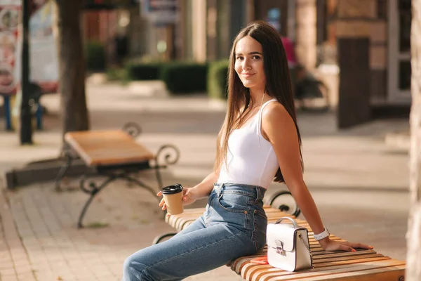 Morena agresiva sentada sola en el banco en el centro de la ciudad. Hermosa joven bebiendo café al aire libre. Fin de la cuarentena. Distancia social — Foto de Stock
