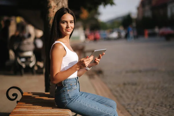 Mooi meisje gebruik tablet buiten. Een vrouw die alleen op de bank zit. Vrouw bekijk video op tablet en glimlach. Ruimte voor tekst — Stockfoto