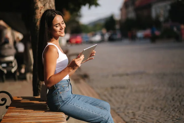 Mooi meisje gebruik tablet buiten. Een vrouw die alleen op de bank zit. Vrouw bekijk video op tablet en glimlach. Ruimte voor tekst — Stockfoto