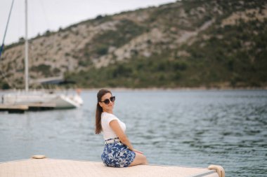 Genç bir kadının deniz kıyısındaki iskelede tek başına oturması. Mutlu kadın.