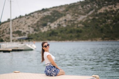 Genç bir kadının deniz kıyısındaki iskelede tek başına oturması. Mutlu kadın.