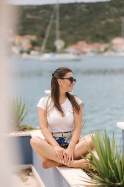 Mavi şortlu, beyaz gömlekli, fotoğrafçı için poz veren güzel bir kadın model. Kadınlar deniz kenarında yalnız vakit geçirir. Mahremiyet yeri