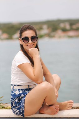 Mavi şortlu, beyaz gömlekli, fotoğrafçı için poz veren güzel bir kadın model. Kadınlar deniz kenarında yalnız vakit geçirir. Mahremiyet yeri