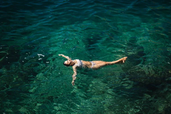 Sexy vrouw in bikini liggend op het water. Aantrekkelijke jonge vrouw die geniet van de zomerzon. Prachtige lagune. Een vrouw zwemt in de zee. Bovenaanzicht — Stockfoto