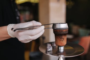 Hookahman Up kömürü nargileye yakın. Parlak elbiseli adam nargile için cımbız kullanıyor.