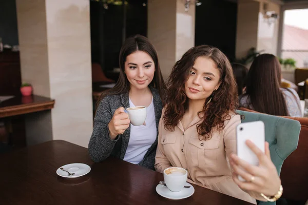 Attraktive junge Frauen machen Selfie im Restaurant. Frauen drin Cappuccino auf der Terrasse. Zwei Weibchen machen gemeinsames Foto — Stockfoto