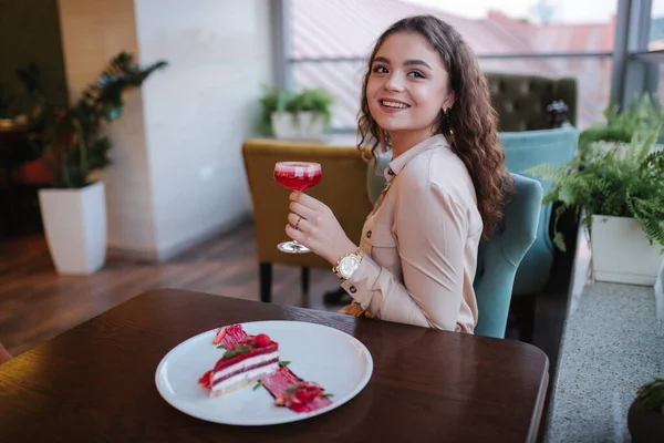 Young woman in restaurant order sweet strawberry cake and red cocktail