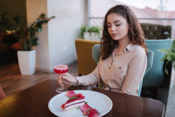 Young woman in restaurant order sweet strawberry cake and red cocktail