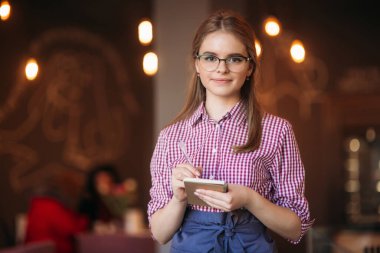 Güzel bir garsonun portresi. Gözlüklü, not kağıdı ve kalemle siparişinizi almaya hazır.