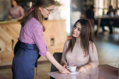 Garson, kafedeki müşteriye kahve ikram ediyor. Mutlu genç kadın, düzeni sağla ve gülümse. kapuçino