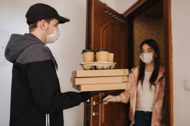 Maskeli ve eldivenli müşterilere pizza ve kahve getiren adam. Kadın kapıyı aç ve siparişi al. Coronavirus teması