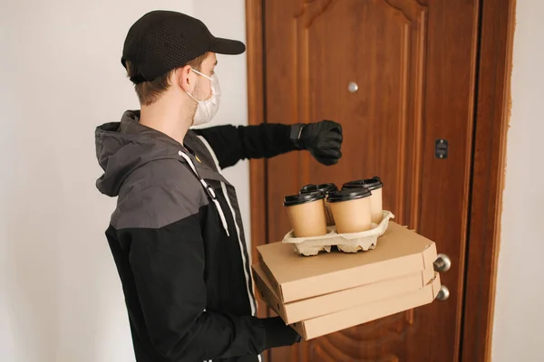 Man delivery pizza and coffe to customer in mask and gloves. Coronavirus theme. Man knocking on doors. And looking at the watch