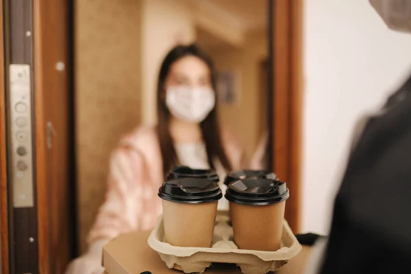 남자가마스크와 장갑을 끼고 피자와 커피를 고객에게 배달합니다. 여자는 문을 열고 질서를 잡는다. 코로나 바이러스의 테마 — 스톡 사진