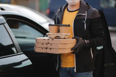 Koruyucu maskeli kurye ve tıbbi eldivenler arabadan sipariş alır. Teslimatçı çocuk pizza ve kahve getirdi. Teslimat servisi karantina altında. Coronavirus covid-19 teması