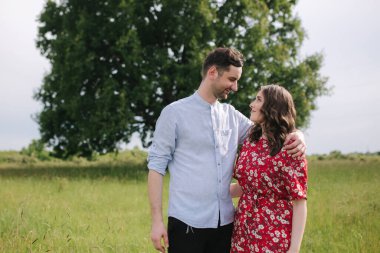 Büyük ağacın önünde yürüyen genç bir çift. Mutlu adam ve kadın birlikte zaman geçiriyorlar. Kırmızı elbiseli kadın.