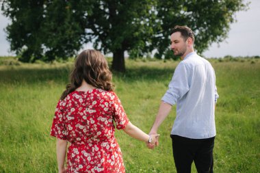 Büyük ağacın önünde yürüyen genç bir çift. Mutlu adam ve kadın birlikte zaman geçiriyorlar. Kırmızı elbiseli kadın.