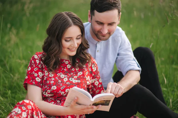 Jovem casal senta-se no plantio ao ar livre e ler livro no mini piquenique — Fotografia de Stock