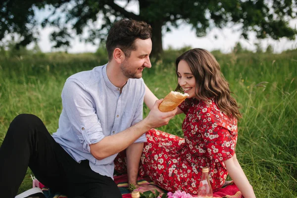 Mutlu erkek ve kadın çifti kırmızı battaniyeye oturur. Kadın ekmeği. — Stok fotoğraf