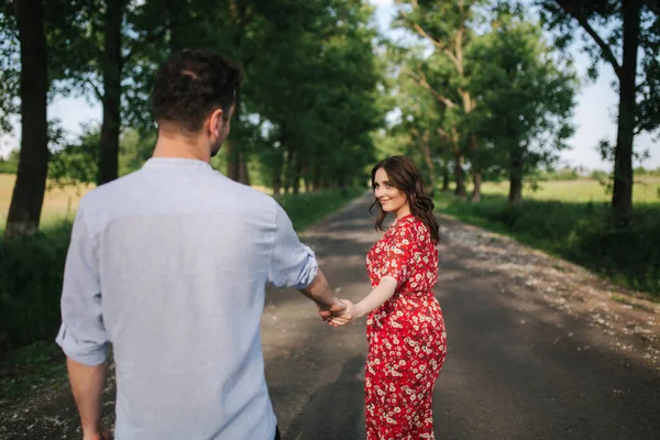 Woman lead her boyfriend outdoors. Beautiful young woman in red dress — Stock Photo, Image