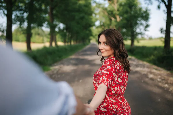 Woman lead her boyfriend outdoors. Beautiful young woman in red dress — Stock Photo, Image