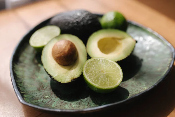 Avocado and lime halves on green plate. Vegetarian food concept — Stock Photo, Image