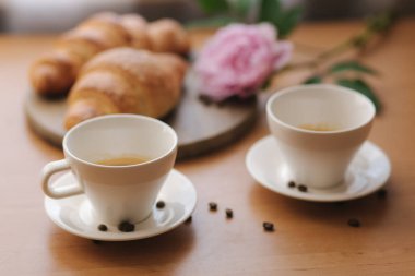 Evde vejetaryen kahvaltısı. Hindistan cevizi sütlü kapuçino ve iki boş vegan kruvasanı. Kahveli sabah. Masada pembe şakayık çiçeği