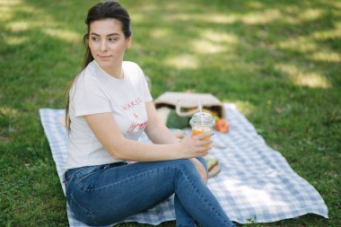 Açık havada piknikte tek kullanımlık portakallı limonata içen bir kadın. Mesaj için yer var. Vegan piknik konsepti