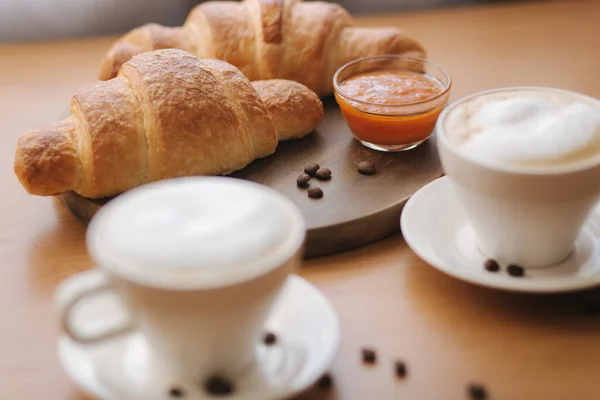 Morgens Kaffee und Croissant auf dem Holztisch. Cappuccino mit frisch gebackenem Knäckebrot nach Hause. Leeres Croissant auf Holzbrett. Marillenmarmelade — Stockfoto