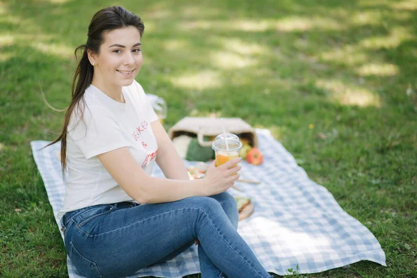 Açık havada piknikte tek kullanımlık portakallı limonata içen bir kadın. Mesaj için yer var. Vegan piknik konsepti