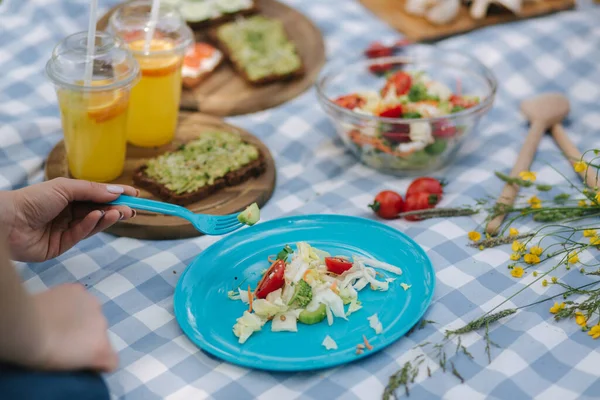 女人在户外野餐时从蓝色盘子里取出沙拉.新鲜健康的食物 — 图库照片