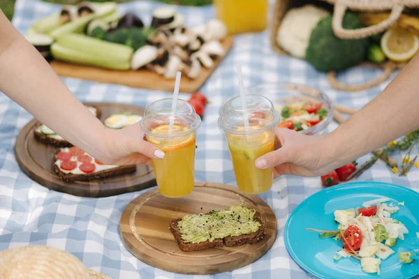 照片中，两只手拿着橙子柠檬水在户外素食野餐前。健康食品概念 — 图库照片