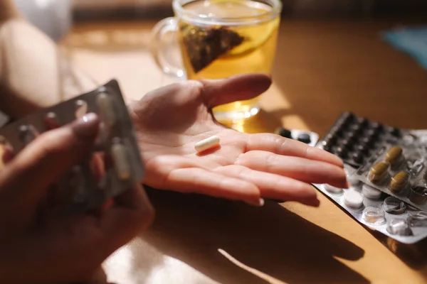 Detailní záběr ženských rukou drží pilulky. Ruku s prášky a černý čaj s citrónem. Imunita. Vitamíny — Stock fotografie