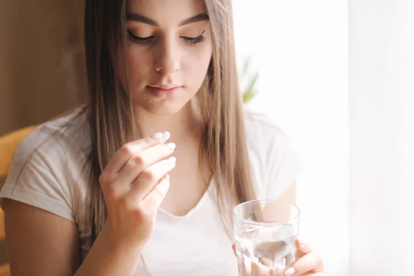 Egy nő portréja, amint tablettákat eszik. Nő otthon a karanténban. Elszigeteltség. A segítőkész nő vitaminokat szed — Stock Fotó