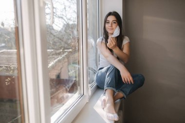 Genç kadın koruyucu maskeni çıkar. Beyaz tişörtlü ve beyaz tıbbi maskeli bir kadın. Karantina sona erdi. Coronavirus teması