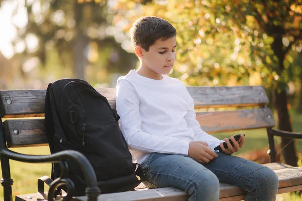 Školák používá telefon v parku po hodině. Mladík používá venku smartphone. Zlatý podzim — Stock fotografie