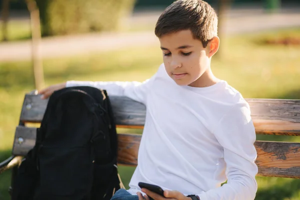 放課後、少年は公園で電話を使う。10代の少年は外でスマートフォンを使う。黄金の秋 — ストック写真