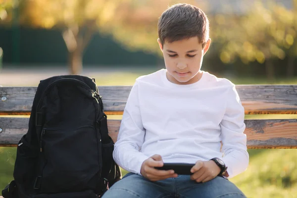 十几岁的男孩在学校下课后在公园里用智能手机玩网络游戏 — 图库照片