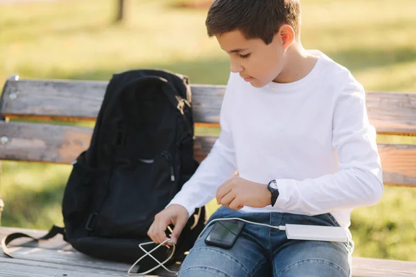 Bello adolescente prendere dal suo zaino powerbark per la ricarica dello smarphone. Carino ragazzo nel parco in autunno — Foto Stock