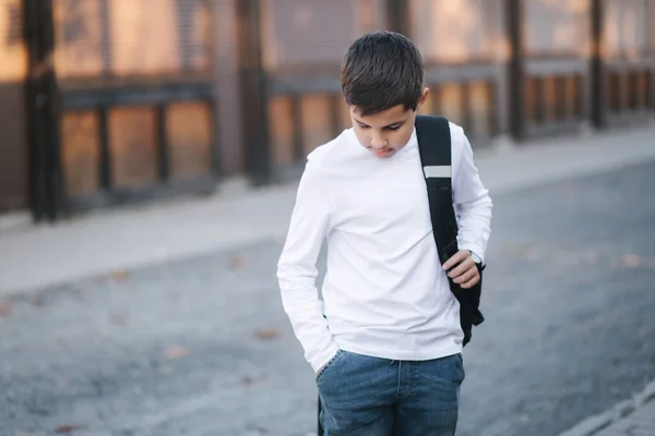 Rapaz adolescente tirar um fone de ouvido sem fio e colocar, em seguida, nos ouvidos. Jovem de camisa branca com mochila. Rapaz ouve música — Fotografia de Stock