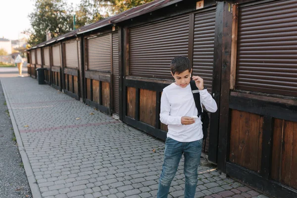 Un adolescente saca unos auriculares inalámbricos y ponlos en las orejas. Niño de camisa blanca con mochila. Boy escuchar música — Foto de Stock