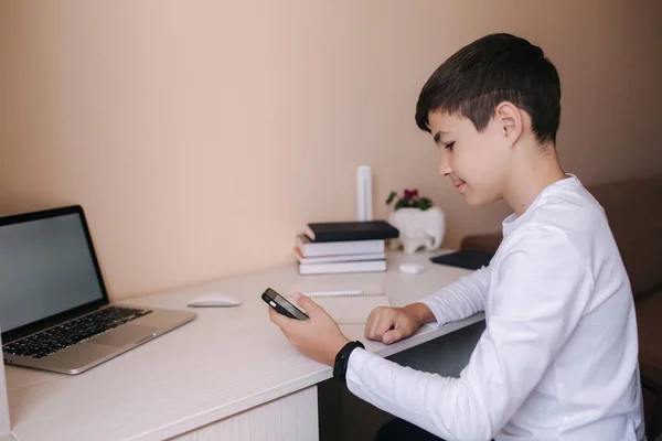 Schooljongen studeert aan een bureau in zijn kamer. Jongen gebruikt laptop voor lessen. Drink thee. Boeken en tablet op tafel. Onderzoek thuis tijdens qurantine — Stockfoto