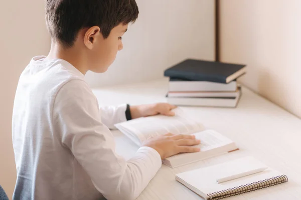 Jonge jongen zit aan het bureau lees het boek en whright neer in notebook. Studie thuis tijdens quarantaine — Stockfoto